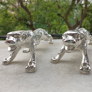 May include: Two silver metal leopard figurines, each with a detailed textured surface, are posed in a crouching position with their heads facing forward.