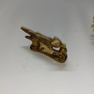 Può includere: Un batacchio per porta in metallo dorato a forma di volpe che tiene una palla nella bocca. Il batacchio è montato su una base rettangolare.