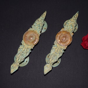 Op de afbeelding: Twee sierlijke, decoratieve deurgrepen met een bloemmotief. De grepen zijn gemaakt van metaal en hebben een groene en gouden afwerking.