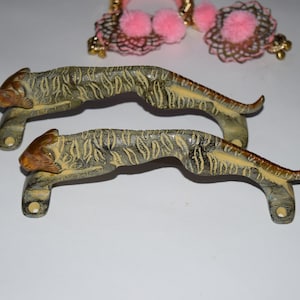 May include: Two antique brass door handles shaped like crouching tigers. The handles have a textured, aged finish and are detailed with stripes.