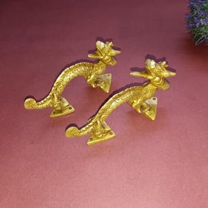 以下が含まれることがあります： 複雑なディテールが施された、金色のドラゴンの形のドアノブが2つ。ノブは、尻尾が巻き上げられたドラゴンの形をしています。三角形のベースに取り付けられています。