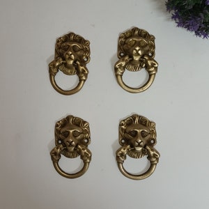 May include: Four antique brass lion head door handles with a ring pull. The lion heads are detailed with a textured finish and have a realistic appearance.