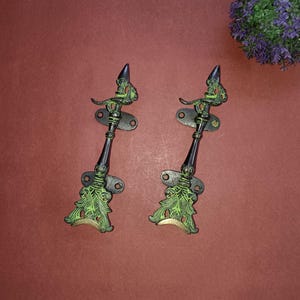May include: Two ornate black and green metal door handles with a decorative design. The handles have a pointed top and a floral design at the bottom.
