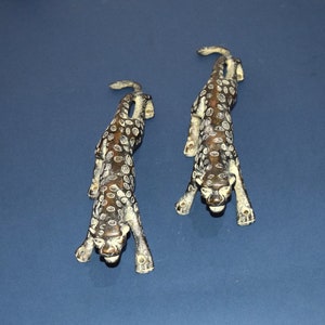 May include: Two black and white leopard figurines with white spots. The figurines are made of metal and have a distressed finish. They are posed in a crouching position with their heads facing forward.