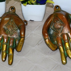May include: Two ornate brass hands with intricate designs, one hand is facing up and the other is facing down. The hands are a dark brown colour with gold accents.