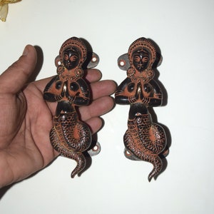 Puede incluir: Un par de tiradores de puerta decorativos hechos de latón. Cada tirador presenta una mujer con cola de serpiente en posición de oración. Los tiradores son negros con acentos rojos.