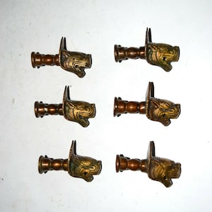 Könnte beinhalten: Sechs antike Messing-Tierkopf-Abschlüsse mit einem detaillierten Design. Jeder Abschluss hat eine zylindrische Basis und einen geschnitzten Tierkopf mit offenem Maul.