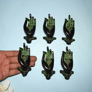 May include: Six black metal hand-shaped door knobs with green patina and gold accents. The hands are in a gesture of giving or receiving.