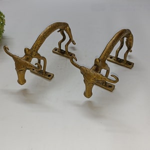 May include: Two gold-toned metal door handles shaped like stylized animal figures. The handles are arched and have a detailed design.