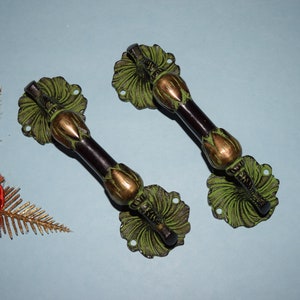 May include: Two ornate green and gold door handles with a black metal bar. The handles have a floral design and are made of metal.