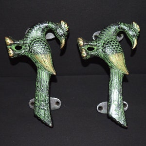 Könnte beinhalten: Ein Paar verzierte Türgriffe in Form von Pfauen aus Messing mit einer grün-goldenen Oberfläche. Die Griffe sind wie Pfauen geformt, mit dem Kopf zur Seite gedreht und dem Schwanz ausgebreitet.
