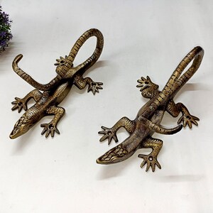 May include: Two bronze-effect lizard-shaped handles. The lizards have detailed scales and curled tails, with their front legs extended. These handles are likely for furniture or doors, adding a unique, artistic touch to home decor.