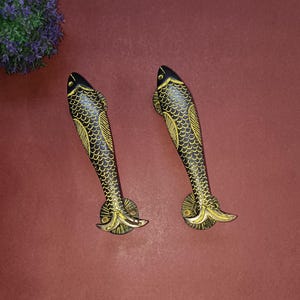 Op de afbeelding: Twee zwarte en gouden deurgrepen in de vorm van een vis. De grepen zijn gemaakt van metaal en hebben een gedetailleerd ontwerp.