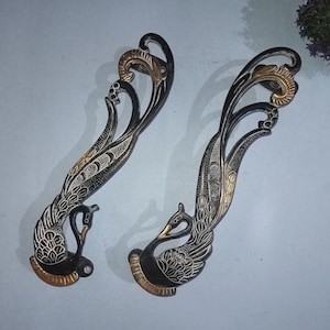 Könnte beinhalten: Zwei verzierte schwarze und goldene Türklinken in Form von Pfauen mit aufwendigen Details.