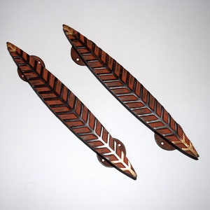 May include: Two brown and black leaf-shaped door handles with gold accents. The handles have a chevron pattern.