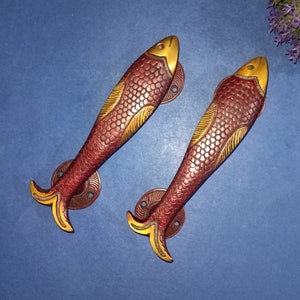 May include: Two ornate brass door handles shaped like fish with red and gold accents. The handles are detailed with scales and have a traditional design.