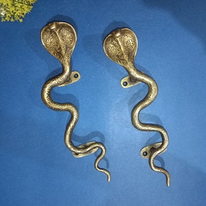 May include: Two ornate brass door handles shaped like snakes with detailed carvings. The handles are a gold color and have a traditional design.