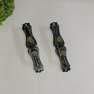 May include: Two black metal door handles with green and gold accents. The handles have a decorative design and are suitable for a variety of doors.