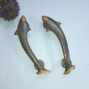 Op de afbeelding: Een paar antieke messing deurgrepen in de vorm van een vis met groene en gouden accenten.