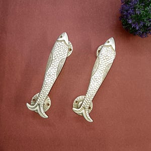 May include: Two silver fish-shaped door handles with detailed scales and a circular base. The handles are on a red background.