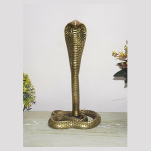 Może przedstawiać: Złota rzeźba kobry z uniesionym kapturem. Wąż jest zwinięty z ogonem schowanym pod ciałem.