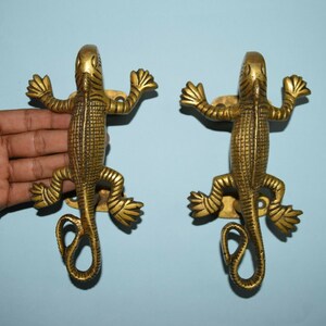 Pode incluir: Um par de puxadores de porta de latão dourado em forma de lagartos. Os puxadores são detalhados com escamas texturizadas e têm uma cauda enrolada.