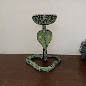 Könnte beinhalten: Ein schwarzer und grüner Kerzenhalter aus Metall in Form einer Kobra mit aufwendigen Details. Der Halter hat eine runde Oberseite und eine gewundene Basis.