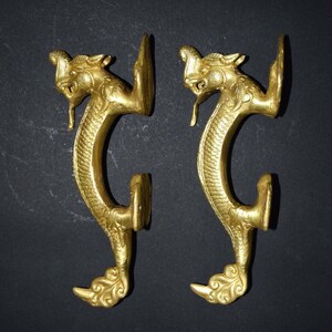 May include: A pair of gold-toned dragon door handles with intricate details. The handles are shaped like dragons with their heads facing forward and their tails curled around the handle.