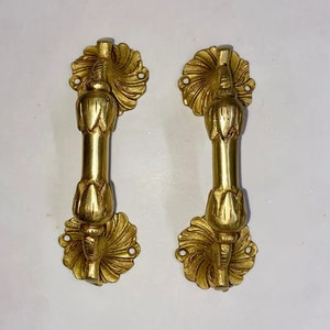 Könnte beinhalten: Zwei verzierte Messing-Türgriffe mit floralem Design. Die Griffe sind goldfarben und haben ein detailliertes, kompliziertes Design.