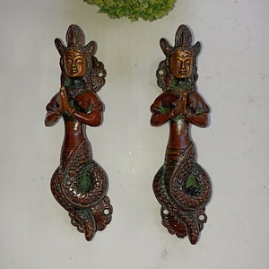 May include: A pair of ornate brass door handles in the shape of a woman with a snake tail. The handles are in a copper and green finish and feature intricate details.