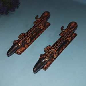 May include: Two black metal door handles with a decorative alligator design. The handles are painted with orange and black details.