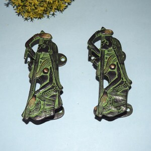 Può includere: Un paio di maniglie per porte in metallo verde con un design decorativo di una donna che suona uno strumento musicale. Le maniglie sono in stile indiano tradizionale.