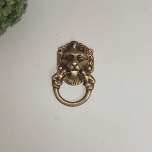 May include: A gold lion head door knocker with a ring pull. The lion's mouth is open and the knocker has a detailed design.