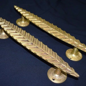 May include: Two gold-toned door handles with a leaf-like design. The handles are made of metal and have a textured surface.
