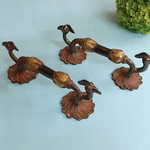 May include: Three ornate brass door handles with a peacock design. The handles are a dark brown color with gold accents.