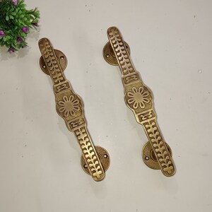 May include: Two ornate brass door handles with a floral design. The handles are a warm gold colour and have a detailed pattern.