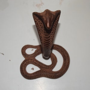 Könnte beinhalten: Eine braune Holzstatue einer Kobra mit erhobener Haube und einem gewundenen Körper. Die Statue ist mit aufwendigen Details geschnitzt und hat eine glatte, polierte Oberfläche.