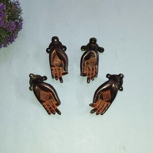 May include: Four antique brass door handles shaped like hands with a diamond pattern in the palm. The handles are a dark brown colour with orange accents.