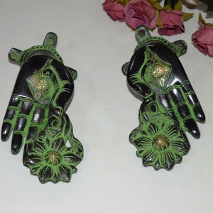 Könnte beinhalten: Zwei grüne und schwarze Wandhaken aus Metall in Handform mit Blumendesign. Die Haken sind mit Schrauben an einer Wand befestigt.