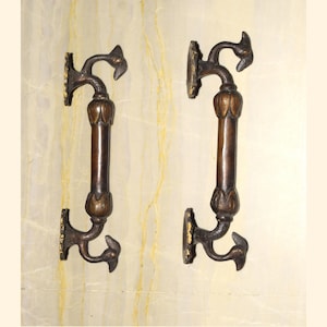 Può includere: Due maniglie per porte in ottone ornate con un motivo a forma di uccello. Le maniglie sono montate su una parete e presentano un motivo floreale decorativo.