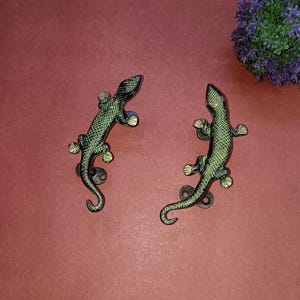 May include: Two green and black lizard-shaped door handles with gold accents. The handles are on a red background.