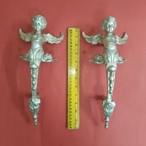 Könnte beinhalten: Zwei silberne Türgriffe in Form von Cherubim mit Flügeln und verzierten Details. Die Griffe sind etwa 25 cm hoch.