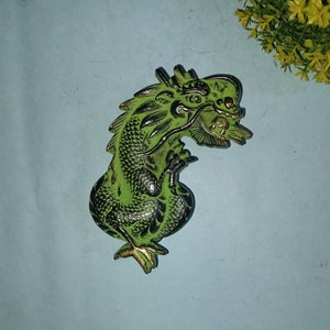May include: A green and black dragon figurine with gold accents. The dragon is curled up in a defensive position with its wings spread out.