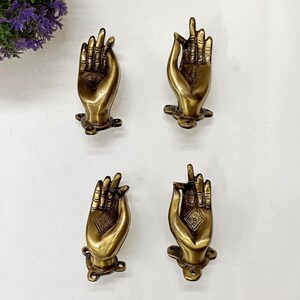 Puede incluir: Cuatro tiradores de armario antiguos en forma de mano, color latón. Cada tirador presenta líneas grabadas y un diseño en forma de diamante en la palma. Los tiradores están montados sobre una pequeña base decorativa.