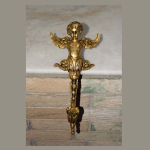 Peut inclure: Un porte-chaussette en métal doré en forme d'ange avec des ailes. L'ange a un visage chérubin et tient un motif floral dans ses mains.