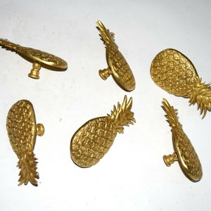 May include: Six gold pineapple-shaped cabinet knobs with a detailed textured surface.
