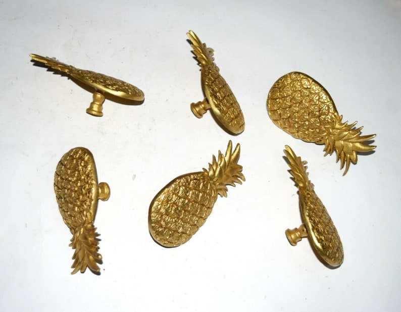 May include: Six gold pineapple-shaped cabinet knobs with a detailed textured surface.