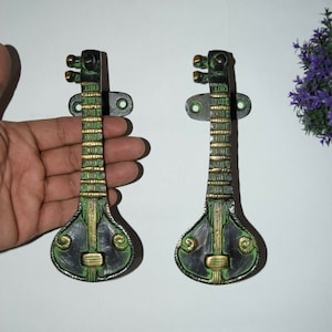 May include: A pair of decorative door handles shaped like a sitar, a traditional Indian musical instrument. The handles are made of metal and have a black, green, and gold finish.