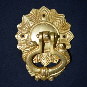 Può includere: Un batacchio per porta dorato con un design floreale decorativo e un'impugnatura ad anello.