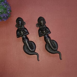 May include: Two black metal door handles shaped like a woman with a snake tail. The woman is in a prayer position with her hands clasped together.
